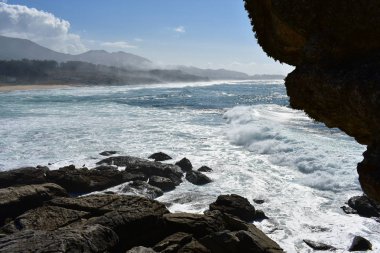 Vahşi deniz kayaların üzerinden. Dalgalar, cliff, köpük, sis, kayalar ve plaj. Galiçya, İspanya. Mavi gökyüzü bulutlu.