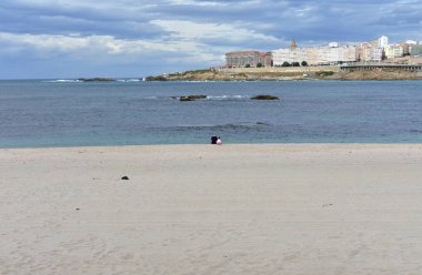 Yaşlı adam ve kumun üzerinde oturan küçük kız ile Riazor plaj. Gün batımı, yağmurlu bir gün, La Coruna, İspanya.