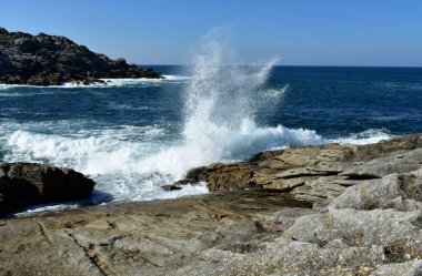 Dalgalar kayalara karşı sıçramasına. Mavi deniz beyaz köpük, güneşli bir gün, açık gökyüzü. Galiçya, İspanya.