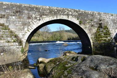 Orman, nehir ve şelale altında bir Ortaçağ taş köprü mavi gökyüzü ile arch. Ponte Maceira, Coruna, İspanya.