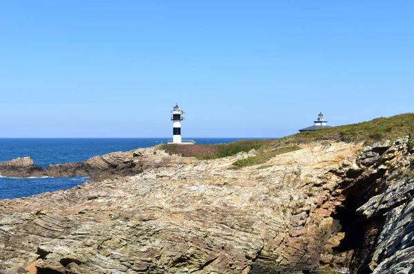 Island with two lighthouses and violet flowers. View from a cliff, sunny day. Isla Pancha, Ribadeo, Spain.