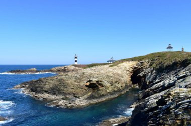 İki deniz feneri ve menekşe çiçekleri ile ada. Bir uçurumdan manzara, güneşli bir gün. Isla Pancha, Ribadeo, İspanya.