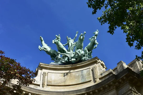 Grand Palais with blue sky. Bronze quadriga sculpture close-up on the top of the building (LHarmonie triomphant de la discorde by Georges Recipon). Paris, France.