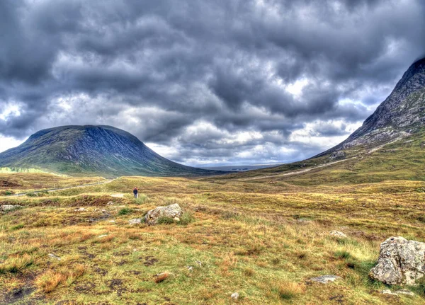 highlands valley of Scotland with mountains, cloud sky and golden meadows at sunset