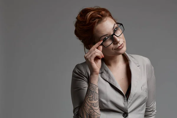 redhead business woman with eye glasses posing on gray background