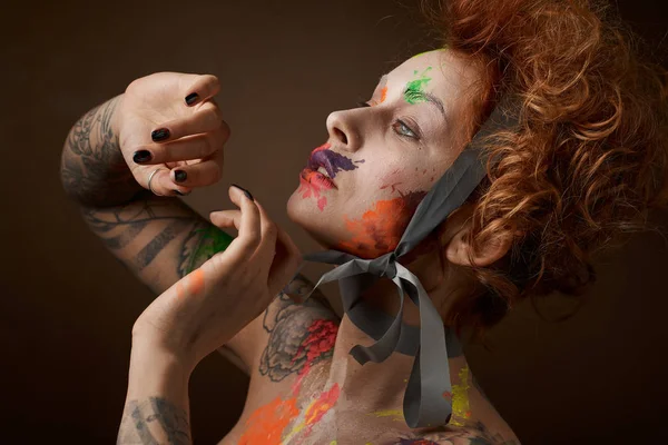 redhead woman with face and body painting on brown background