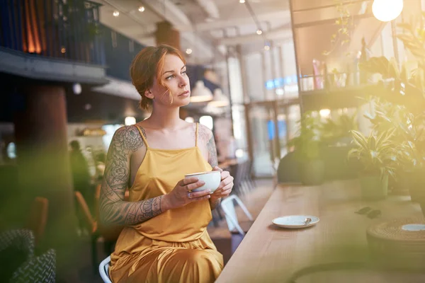 Tattooed ginger woman sitting in cafe and drinking coffee
