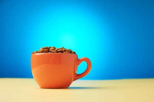 Cup full of coffee beans on blue background