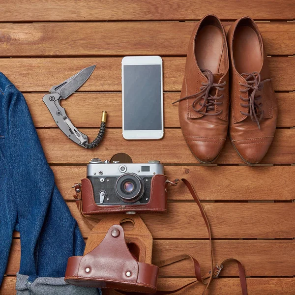 old brown leather shoes, smartphone, knife and vintage camera on wooden background