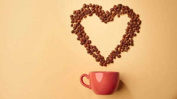 Red cup with heart made with coffee grains on beige background