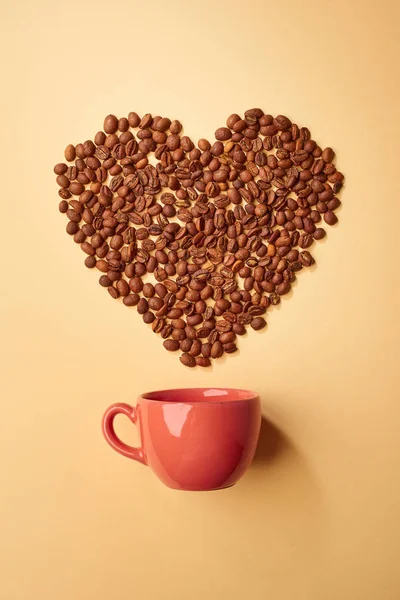 Red cup with heart made with coffee grains on beige background