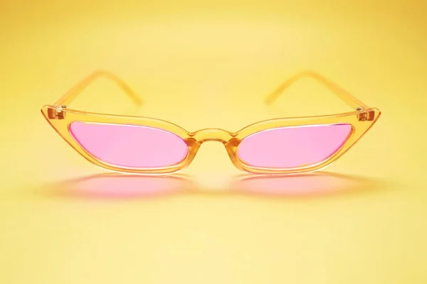Thin glasses with pink lens on bright yellow background