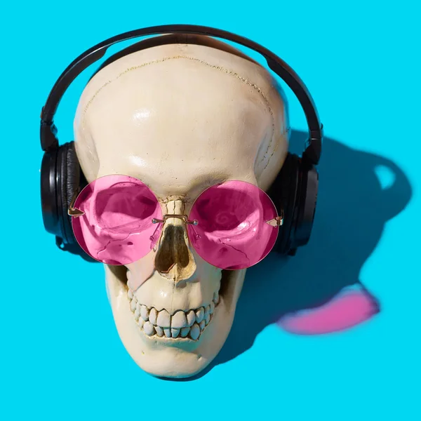 Human skull with headphones and pink glasses on blue background