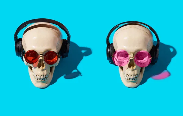 two human skulls with red and pink glasses and headphones on blue background
