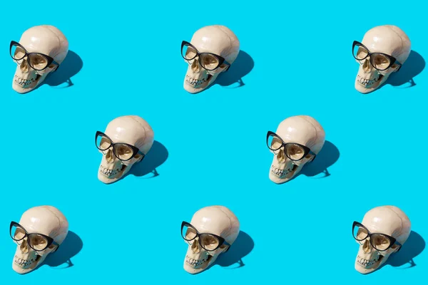 Seamless pattern with human skulls in cat-eye glasses on blue background