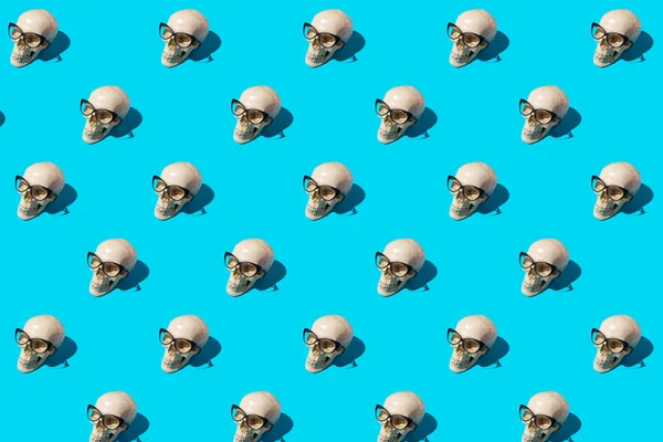 Seamless pattern with human skulls in cat-eye glasses on blue background