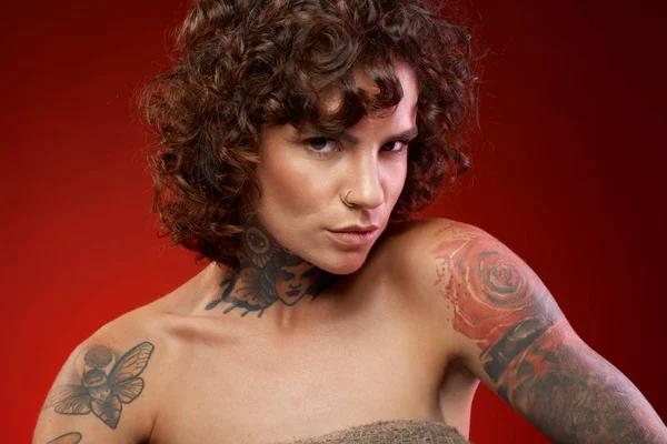 Curly young tattooed woman on red background
