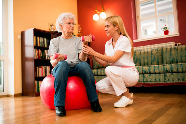 Senior woman workout with dumbbells, nurse helps to patient about exercises