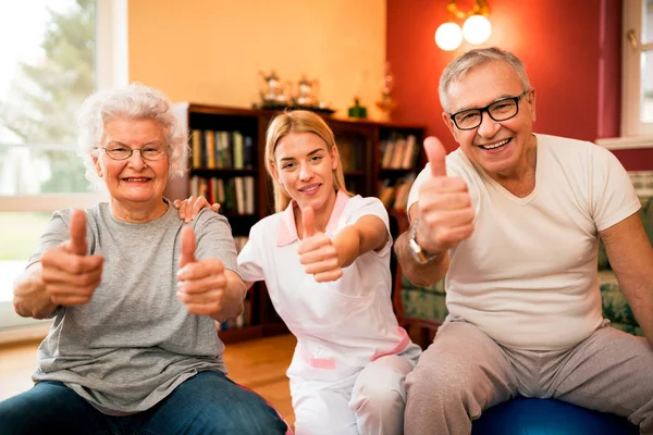 Glücklich Lächelnde Senioren Mit Krankenschwester Zeigt Nach Erfolgreicher Bewegungstherapie Den — Stockfoto