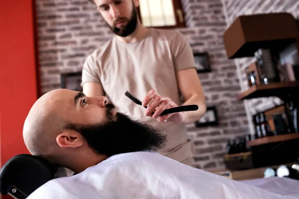 Barber with old-fashioned black razor shaves beard