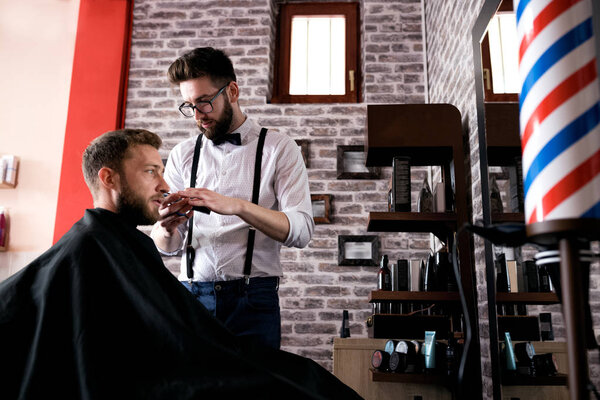 Professional master hairdresser cuts client beard in barbershop salon