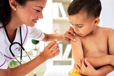 Gentle lady doctor giving a vaccine to one fearless little boy clipart