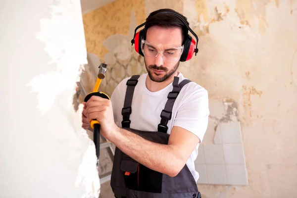 Handyman wearing hearing protection headphones while tearing down wall segments one by one