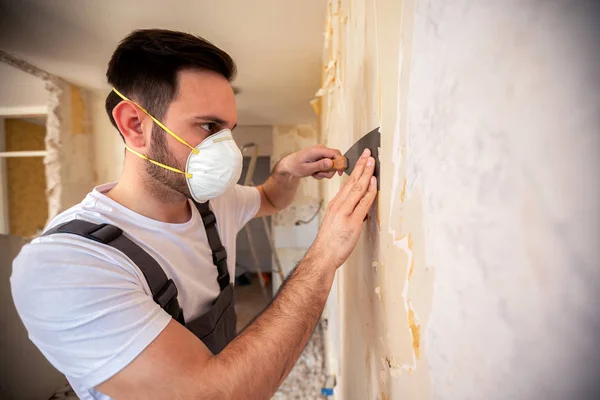 Scraping of wallpaper with a putty knife done by a crafty and a skilled worker