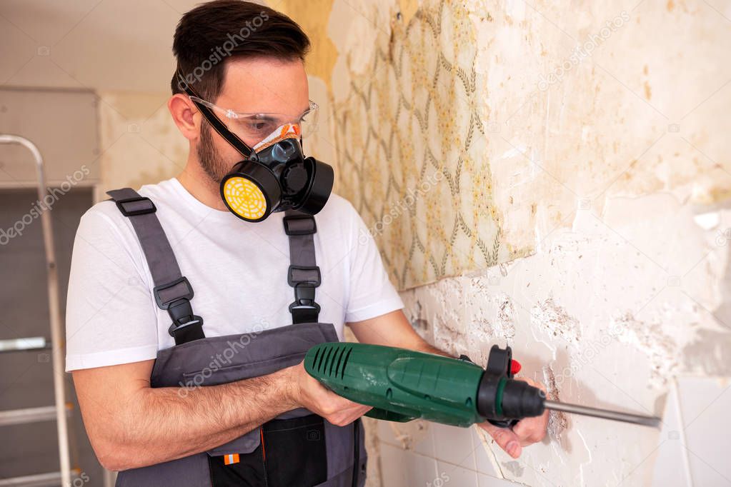 Crafty worker removing porcelain tiles from an old and ruined wall 