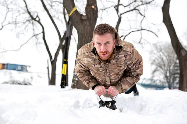 Handsome bearded athlete doing kettlebell push ups on the snow