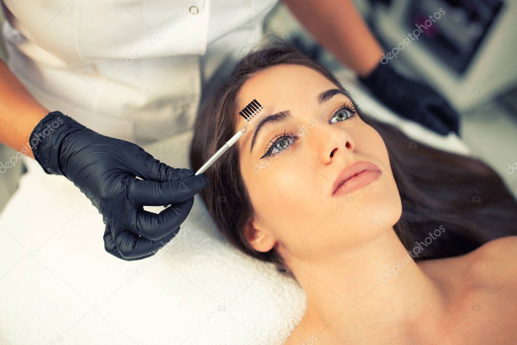 Certified beautician preparing her client eyebrows in order to apply more precise and hair-like strokes