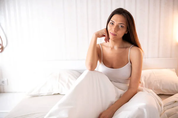 Attractive woman having a lazy morning sitting on the bed and wondering