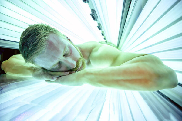 Мускулистый человек в солярии лежит на животе
 