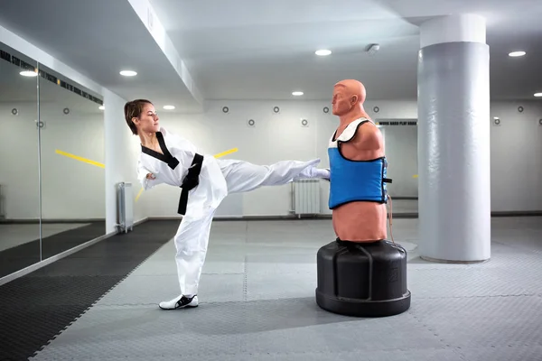Young woman with physical disability performing kicks on a punching dummy, para-taekwondo concept