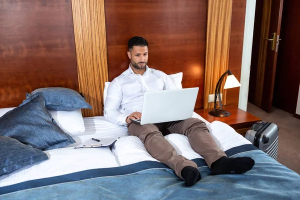 Hombre guapo en la cama con su portátil — Foto de Stock