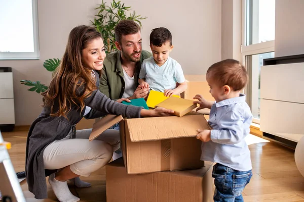 Casal jovem desempacotando caixas com seus dois filhos — Fotografia de Stock
