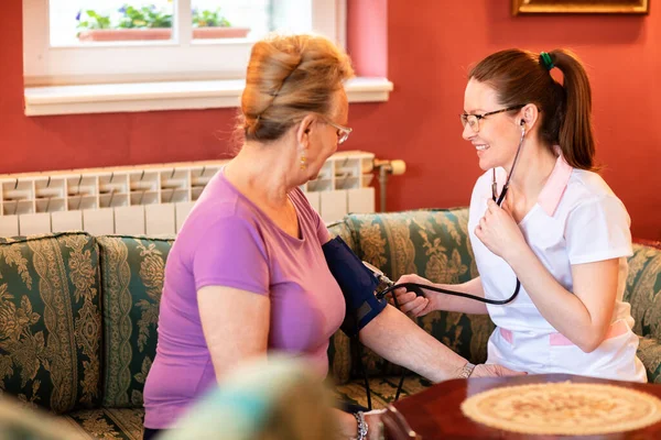 Caring nurse measuring blood pressure of her patient, nursing home