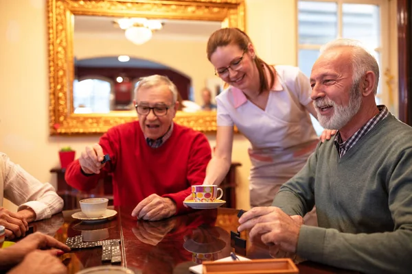 Sjuksköterska Serverar Medan Äldre Människor Spelar Brädspel Äldreboende — Stockfoto