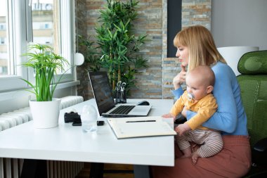 Sorumlu anne çocuğunu kucağında tutuyor ve evde çalışıyor.