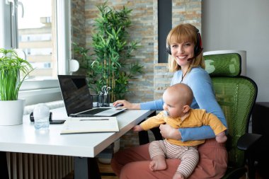 Sorumluluk sahibi bir ebeveyn çalışırken çocuğunu kucağında tutuyor.