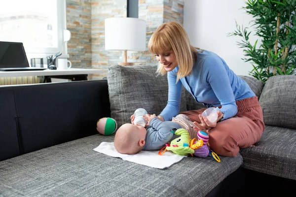 Sevgi dolu anne bebeğine su veriyor. Oturup kanepede uzanırken.