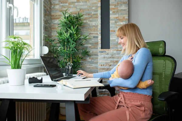 Annesi ve çocuğu ofiste, annesi çalışıyor ve bebeğini kucağında tutuyor.