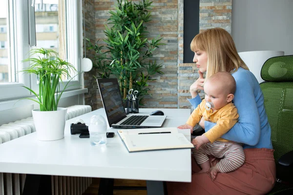 Sorumlu anne çocuğunu kucağında tutuyor ve evde çalışıyor.
