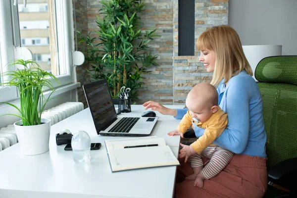 Sorumlu anne çocuğunu kucağında tutuyor ve evde çalışıyor.