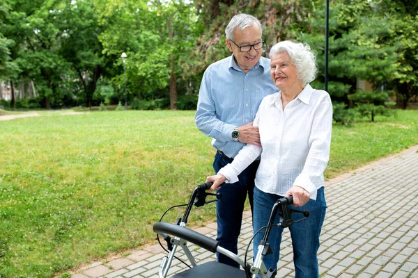 Senior woman strolling with a little help of her husband and walking aid