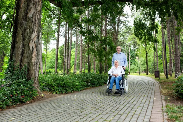 Senior couple together through tough times spending time together in the park, wheelchair concept