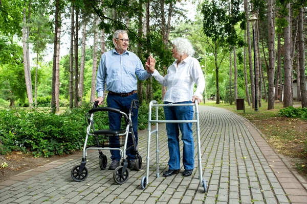 Elderly couple holding on to walking helper with one hand and high five with another