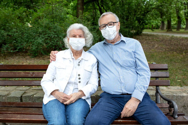 Senior couple with face masks sitting on the park bench, virus protection concept
