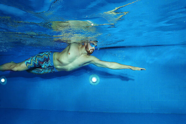 Young man swimming in the swimming pool shot from underwater, swimming concept