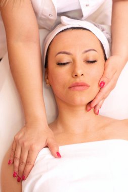 İyi eğitimli bir masözün elleri bir kadının yüzüne masaj yapıyor, yüz masajı konsepti.